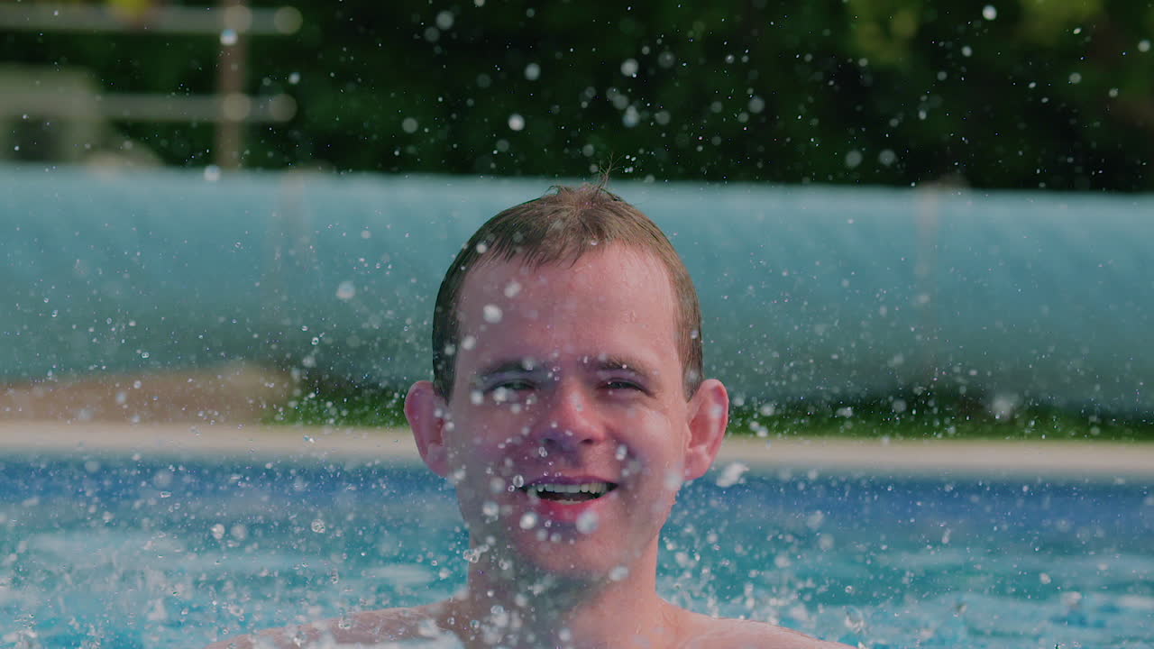 Joven salpicando agua y sonriendo en una piscina.