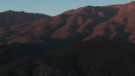 aerial shot as the drone moves upwards to reveal the stunning klein karoo mountains at sunset, western cape, south africa. the dramatic golden light illuminates the rugged landscape at dusk
