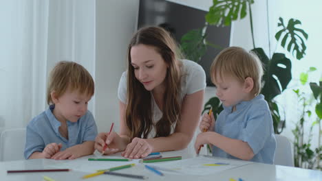 young mom and two sons 2-4 years old draw pencils drawing on boomega sitting at the living room table in slow motion