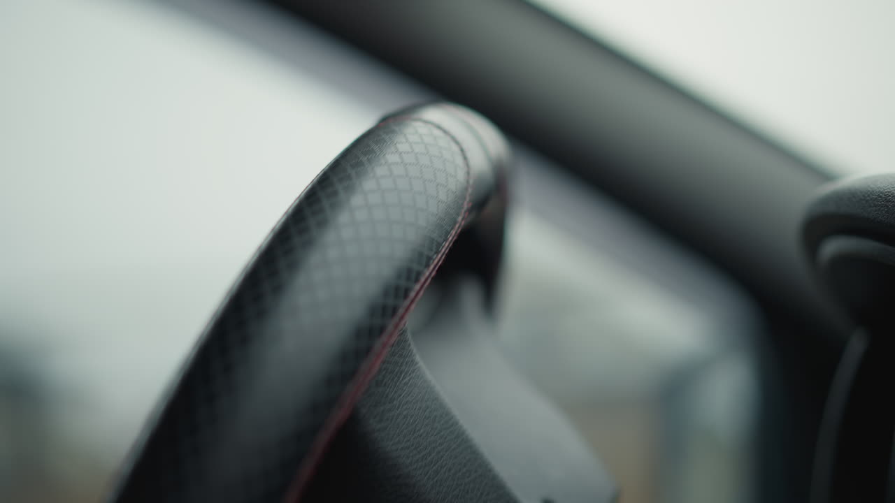 Low angle male hand turning steering wheel with wrist motion, interior view of textured wheel cover and blurred daylight through windshield, emphasizing driver control with smooth confident gesture