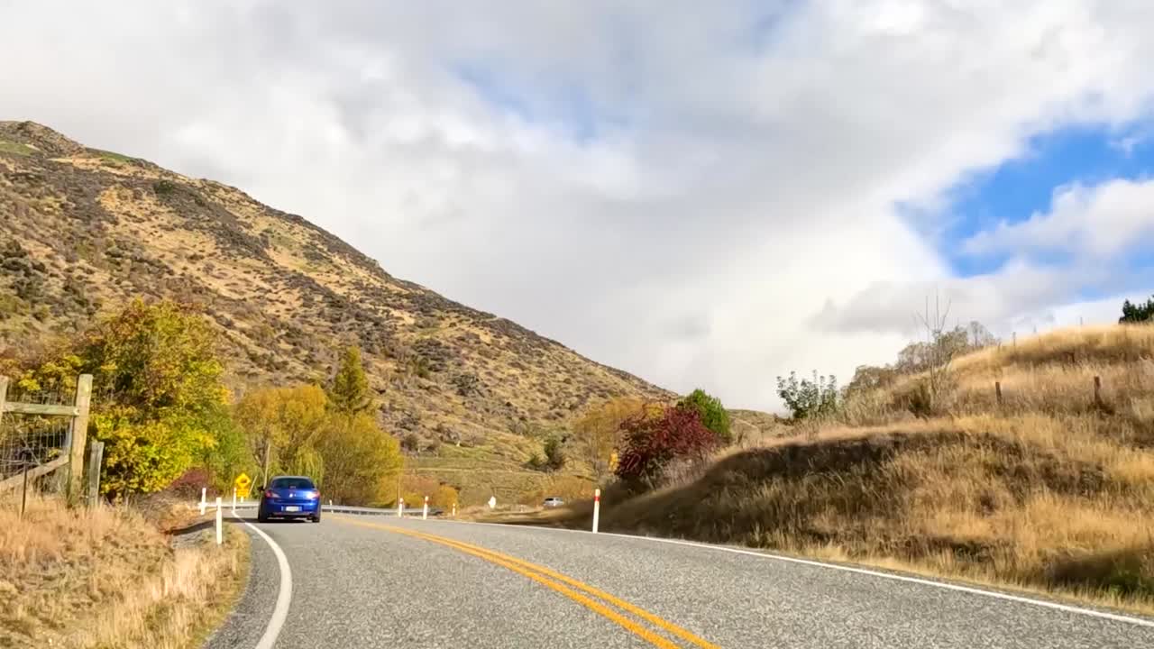 Una perspectiva en primera persona conduciendo a través de un puerto de montaña sinuoso rodeado de vibrantes árboles otoñales.