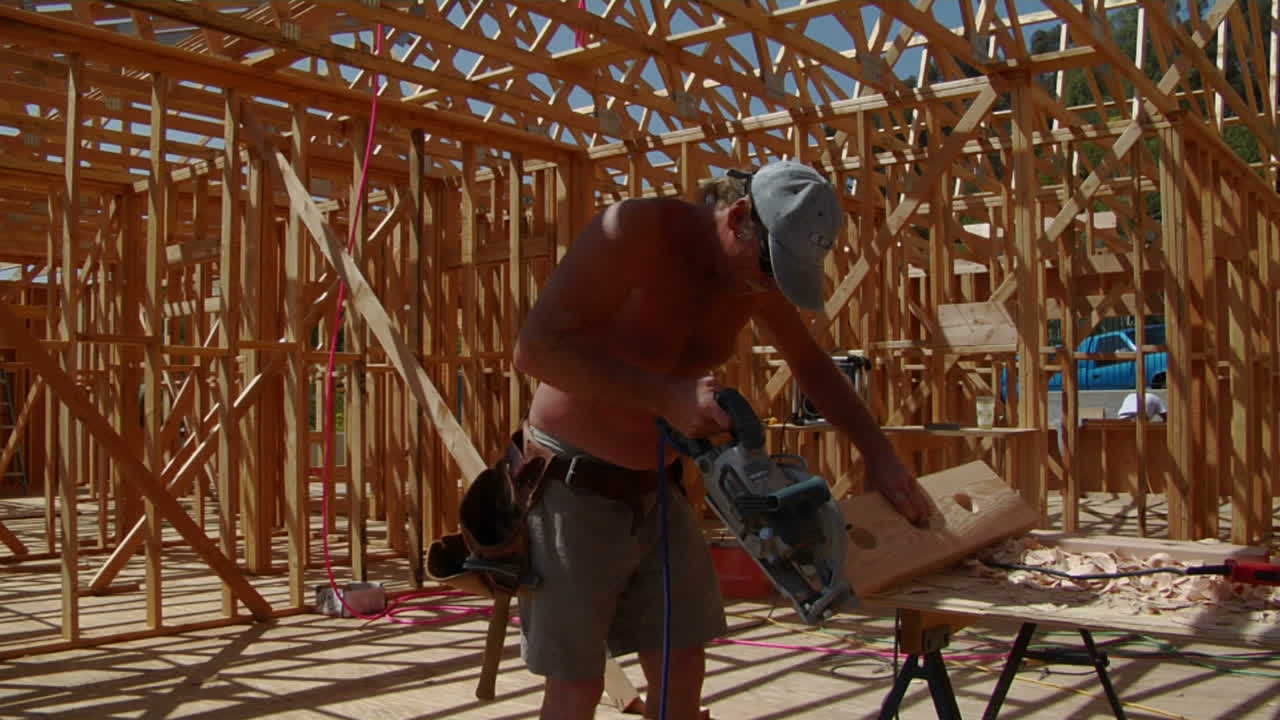 un contratista corta un trozo de madera y luego camina por un balcón sin terminar