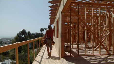 a contractor cuts a piece of wood then walks along an unfinished balcony