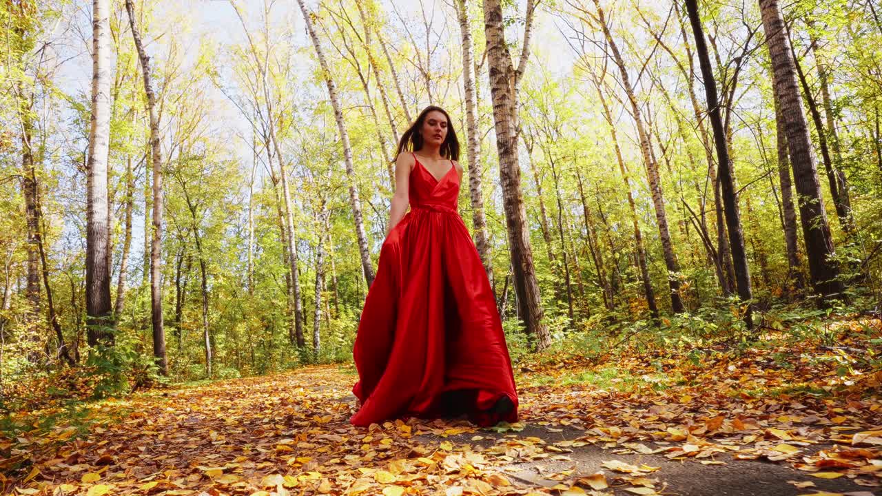 A graceful figure clad in a flowing red gown strolls through a picturesque forest path, surrounded by golden autumn foliage and tall slender trees, capturing the essence of nature's beauty