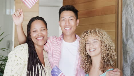 young asian man and two young biracial women pose cheerfully with waving american flags