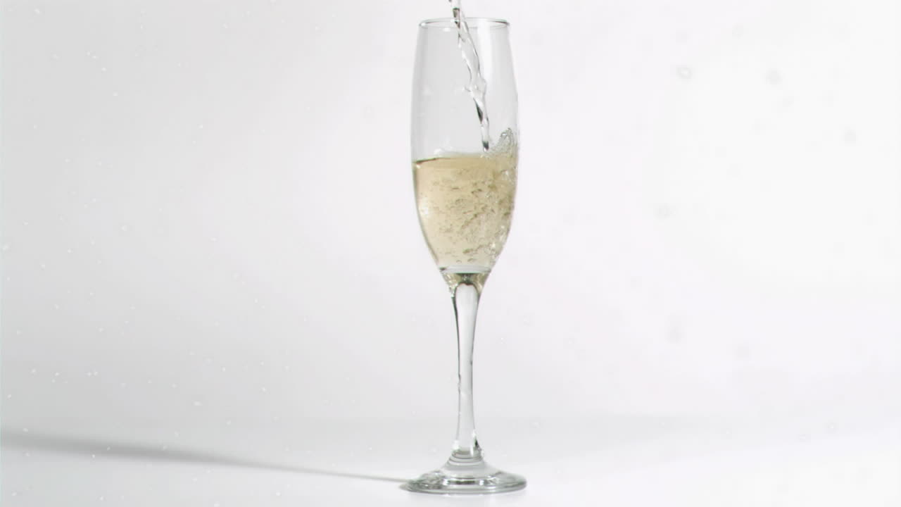 Animation of white specks falling over glass of champagne on white background