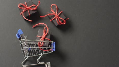tres regalos negros atados con cuerda roja y carrito de compras en fondo negro con espacio de copia