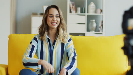 happy female blogger recording a video for her followers sitting on a yellow sofa at home 1