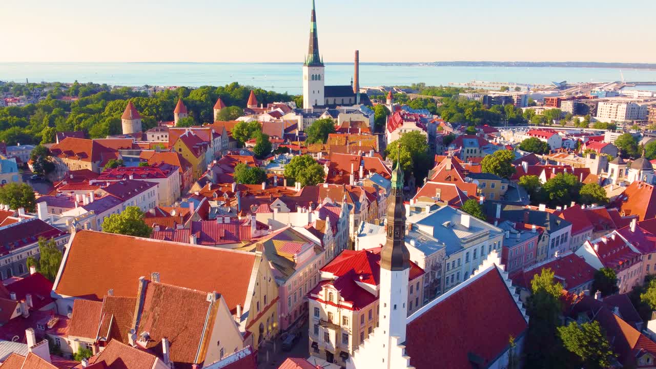 Aerial drone shot of iconic red roofed buildings near St. Olaf's Church tower, with stunning bay view in background at Tallinn, Estonia.