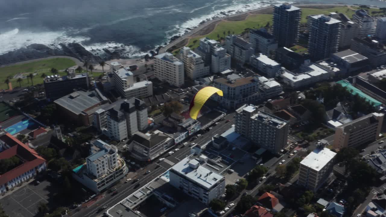 Paraglider flies over city with buildings, roads and traffic beneath. Adventure and adrenaline concept.