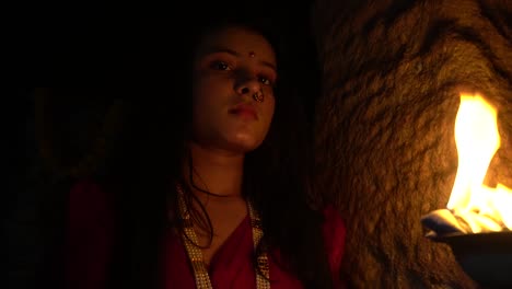 beautiful-Indian-girl-in-old-stepwell-wearing-traditional-Indian-red-saree,-gold-jewellery-and-bangles-holding-fire-plate