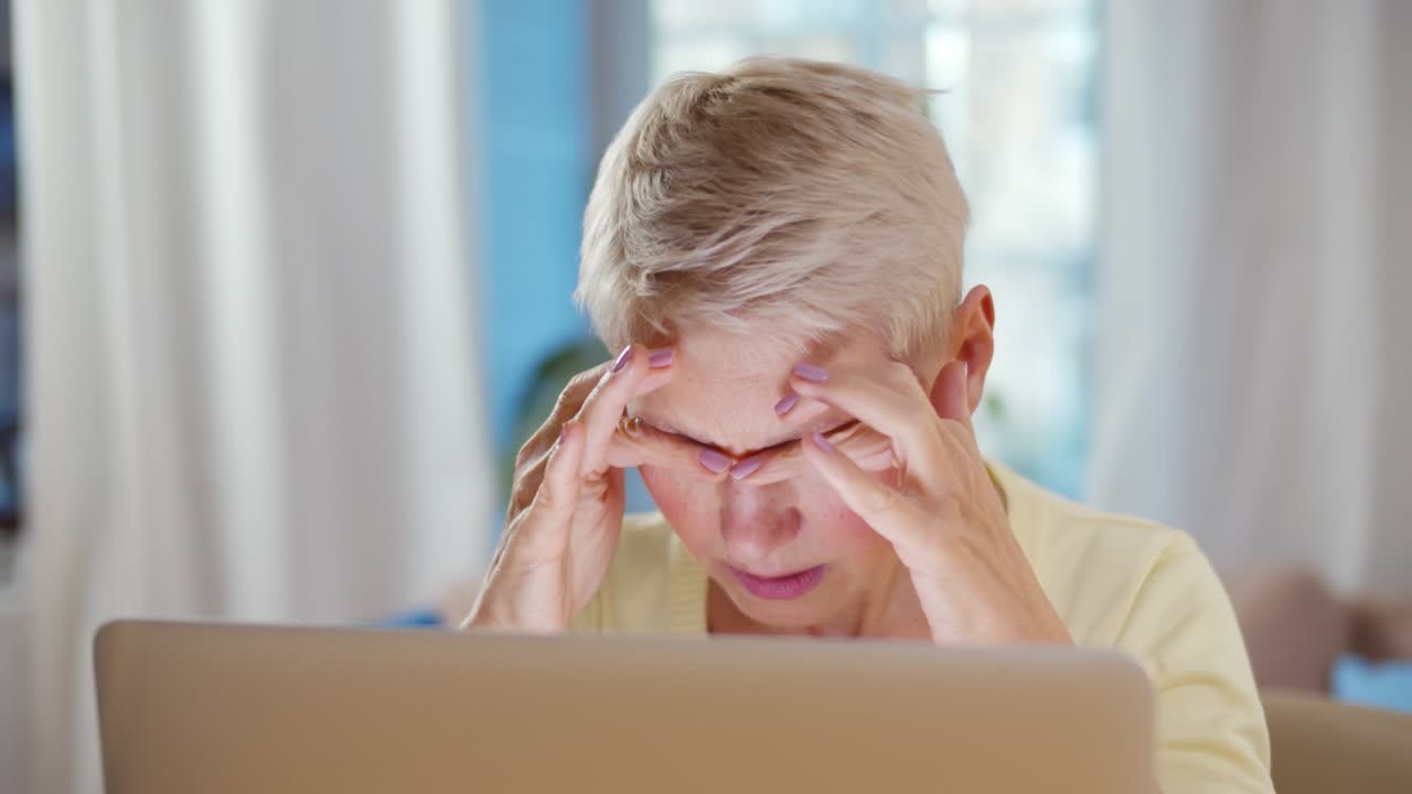 노인 여성이 과 함께 앉아서 일하면서 손으로 머리를 들고 있습니다.