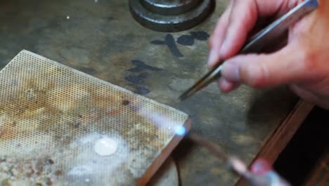 close-up of craftswoman blowing a torch to melt metal