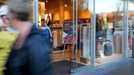 people walking past a shop window displaying winter clothing.