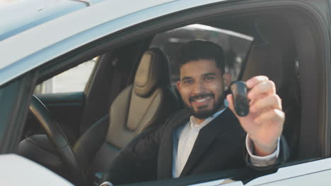 hombre sosteniendo las llaves del coche dentro de un vehículo eléctrico moderno