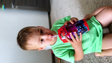 caucasian kid wearing light green t-shirt holding a cup. portrait of a baby boy drinking from a straw. close up. vertical view.