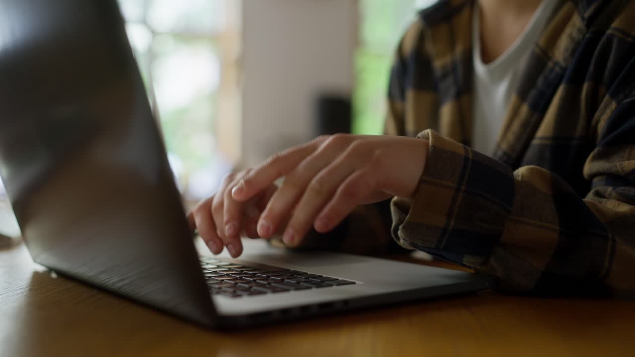 primer plano de una chica con una camisa a cuadros escribiendo en un teclado de portátil mientras está sentada en una mesa en la biblioteca