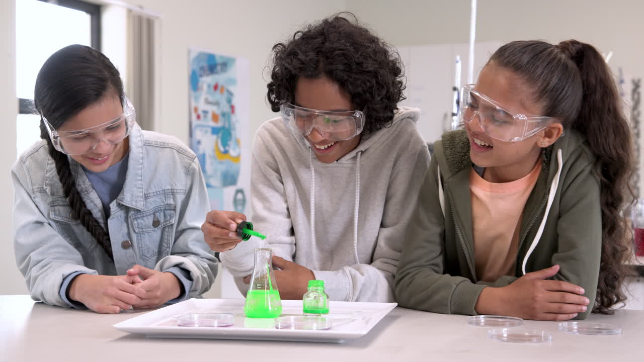 Multiracial students in science class experimenting with green liquid, in safety goggles, at school