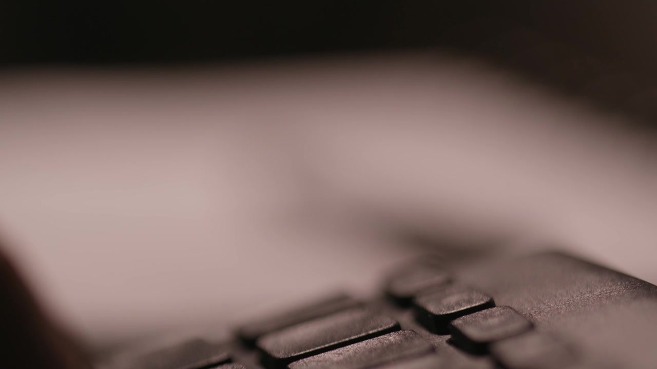 Fingers writing on a keyboard in the blurred foreground with a pen and a notepad in focus in the background.