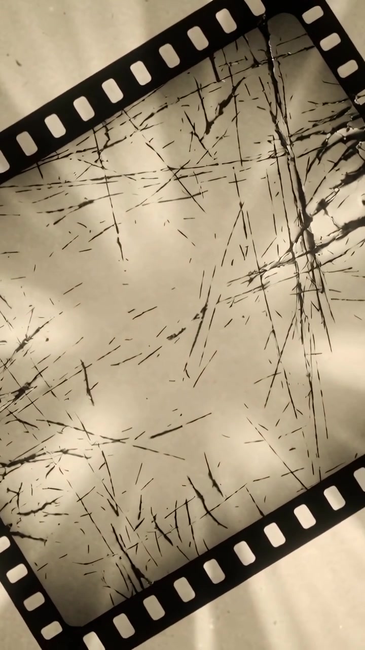 Vídeo vertical: Tira de filme 35mm girando e deslizando na mesa com movimento de câmera, com perfurações e arranhões