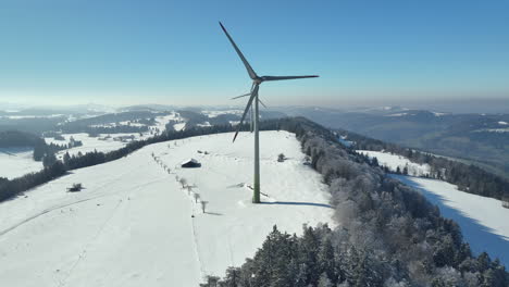 two modern windmills rotating on the top of a with snow covered swiss mountain on a cold sunny winter day