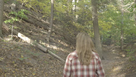 handheld pan down from trees to a young woman walking on a trail in the woods