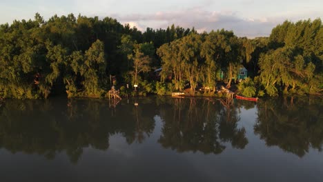 Toma-Aérea-De-La-Hermosa-Selva-Amazónica-Y-Una-Casa-Solitaria-En-La-Orilla-Del-Río-Durante-La-Iluminación-Del-Atardecer