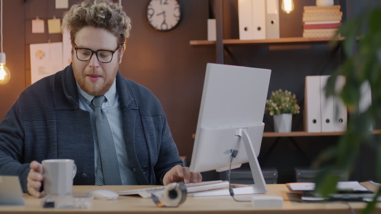 Man Drinking Coffee and Working on Computer in Office
