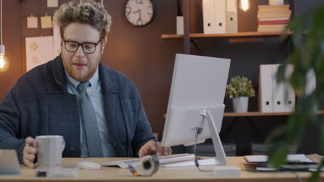 man drinking coffee and working on computer in office