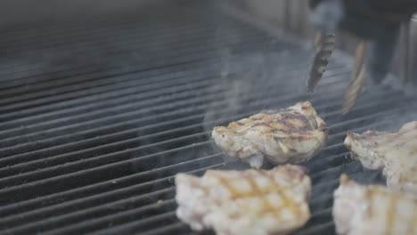 Grilled-chicken-legs-on-barbecue,-turning-with-tongs