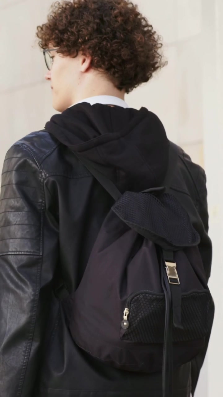 Vertical video: Walking man in jacket glancing left slowing adjusting pack on sidewalk at blue bag