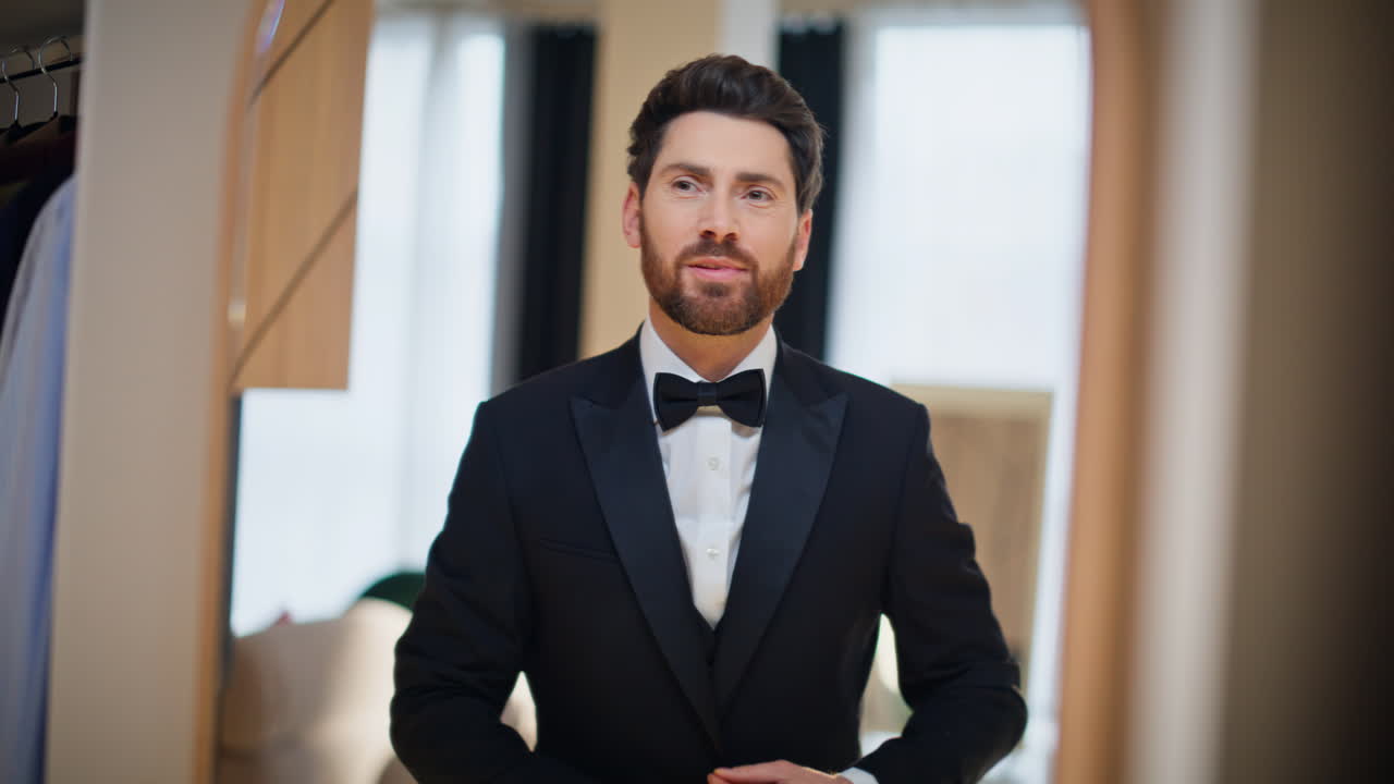 Primo piano di un uomo d'affari barbuto che si allaccia la camicia nella cabina armadio. Uomo che si guarda allo specchio.