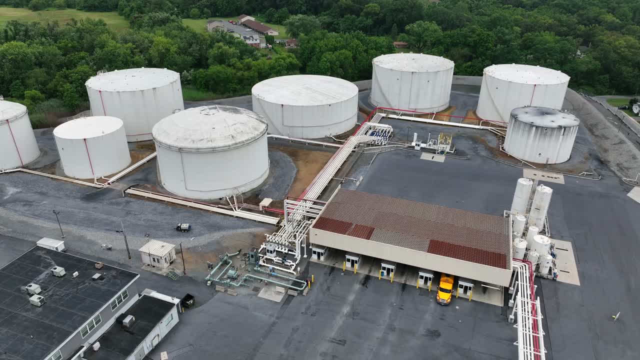 Yellow truck parking at loading ramp for petroleum in American town. Aerial top down. Several tanks with field for aircraft