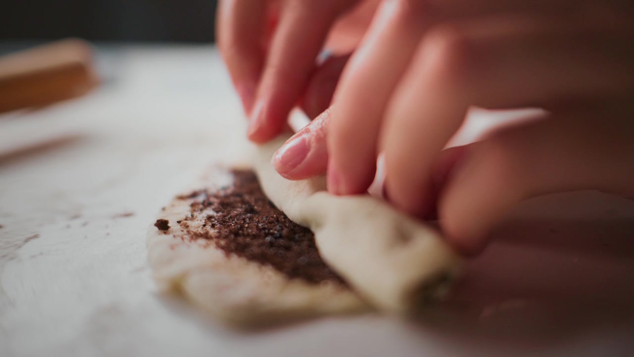 Close-up of hands folding dough with dark filling. Gentle, precise motions show care in food preparation. Scene highlights artisanal baking process. Ideal for recipes, culinary tutorials