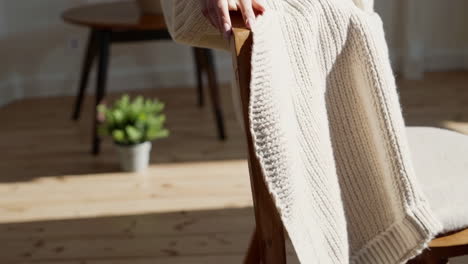 person in a cozy knitted sweater sitting indoors on a wooden chair