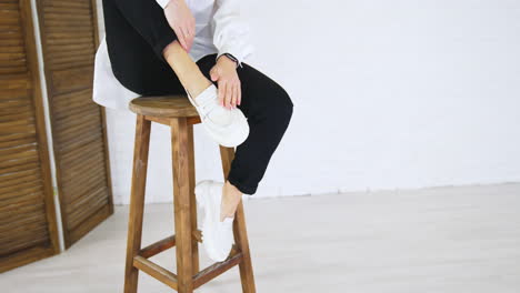 stylish white loafers on the feet of a lady sitting on high stool. model touches the shoes then changes her position. white wall backdrop.