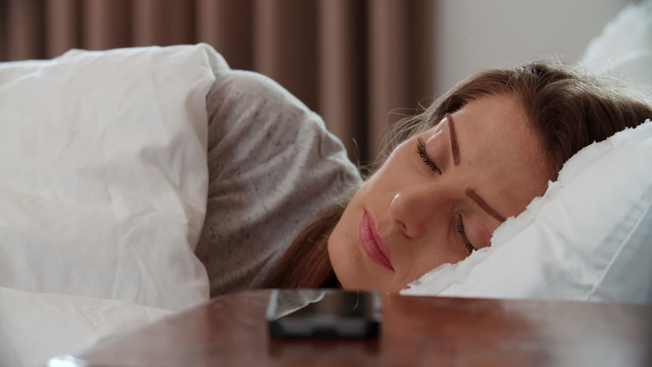 침대에 누워 있는 여자 가 드폰 에 있는 알람 으로 깨어난다