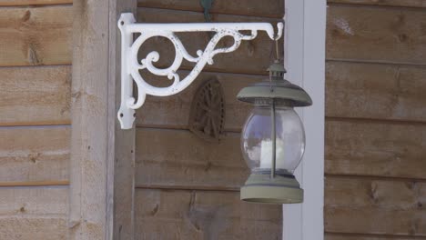 Retro-metal-lantern-with-a-candle-inside,-hanging-from-a-wooden-house-and-swinging-in-the-wind