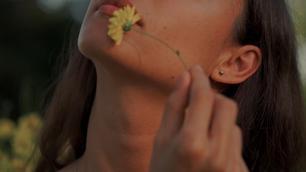 Giovane donna serena che si tocca delicatamente il viso con un fiore giallo