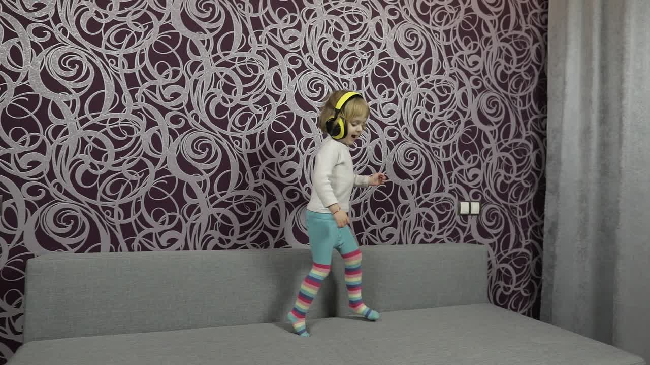 niño feliz saltando y bailando en el sofá y escuchando música en auriculares