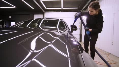 woman blowing off water from freshly washed black car with air.