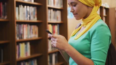 A-smiling-Asian-female-student-wearing-a-yellow-hijab-standing-and-using-a-smartphone