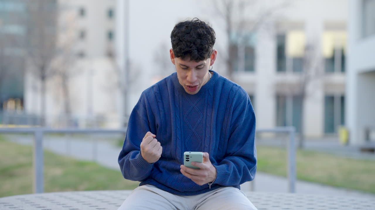 Young man celebrating success on smartphone outdoors