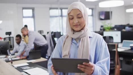 Portrait-of-happy-biracial-businesswoman-using-tablet-with-colleagues-in-office,-slow-motion