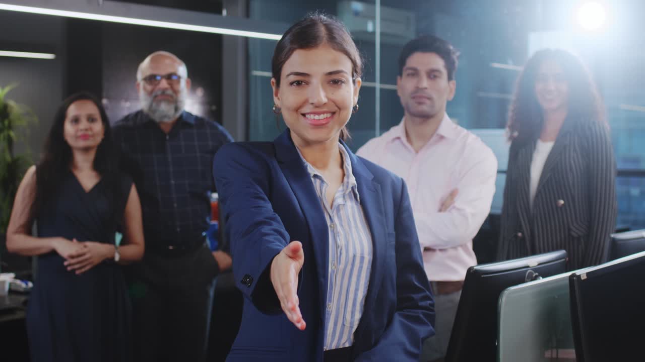 mujer corporativa india extendiendo la mano para un apretón de mano con empleados de género mixto