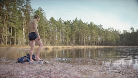 un bañista de hielo musculoso y en forma se quita el poncho y se prepara para entrar al lago congelado