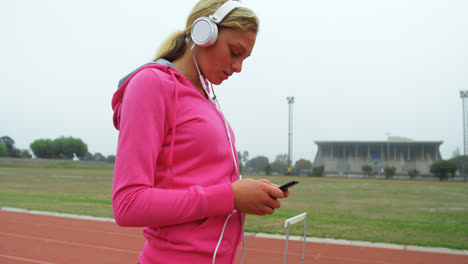 vista lateral de una atleta caucásica escuchando música en el teléfono móvil en un recinto deportivo 4k