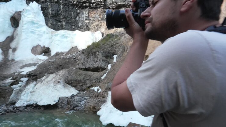 Mandlig eventyrer fotograferer et fantastisk vandfald med dvælende sne i Banff Nationalpark, Canada