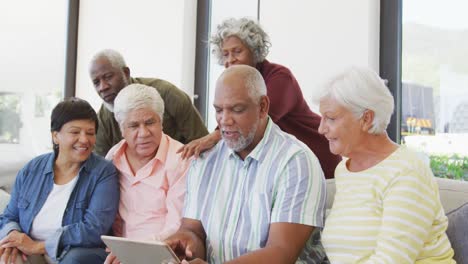 Happy-senior-diverse-people-talking-and-using-tablet-at-retirement-home