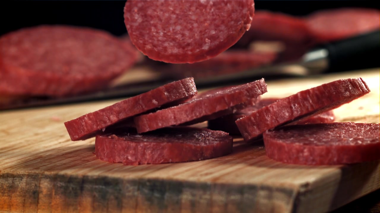 Fette di salame che cadono su un tagliere di legno